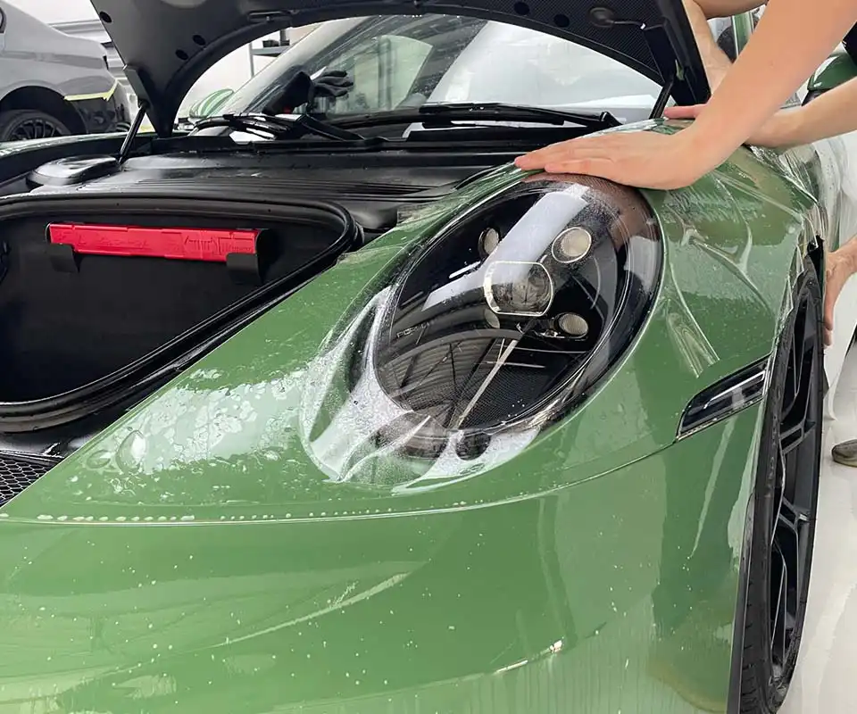 PPF being applied around the headlight of a green Porsche