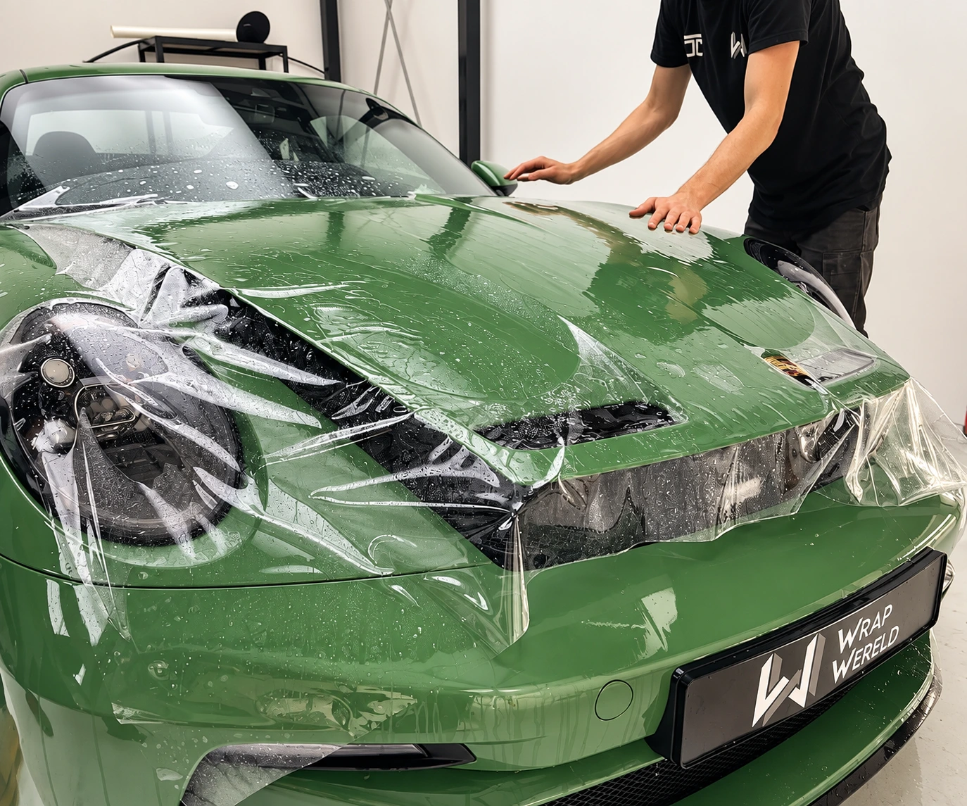 Transparent protective film being applied to a green Porsche